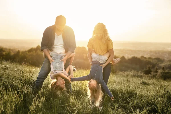 日落时 有两个女儿的家庭在草地上玩得很开心 — 图库照片