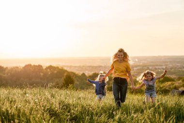 Çayırda koşan iki kızı olan beyaz bir anne.                                