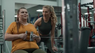 Kilolu bir kadın spor salonunda fitness hocasıyla antrenman yapıyor. 4K 'da kırmızı helyum kamerayla çekildi..  
