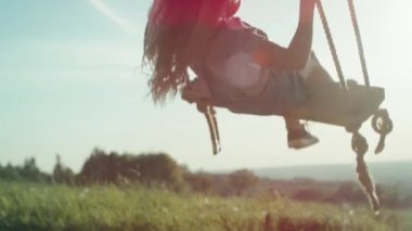 Küçük kız, altın saat boyunca yaz gününün zirvesinde sallanıyor. 4K 'da kırmızı helyum kamerayla çekildi..  
