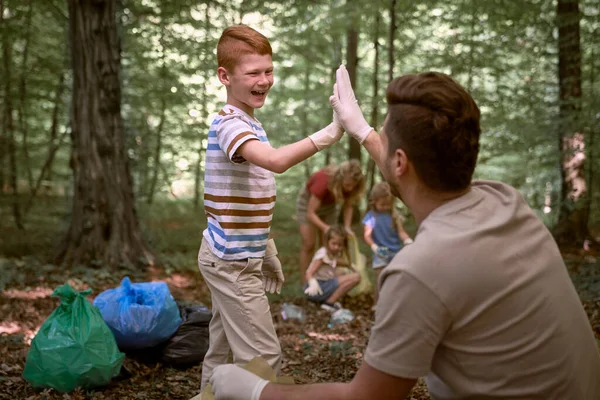 Caucasian boy cleaning forest from trashes with family