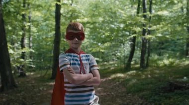 Zencefilli beyaz çocuk süper kahraman kostümü giymiş çöp torbalarıyla dikiliyor. 4K 'da kırmızı helyum kamerayla çekildi..     