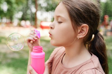 Beyaz kız parkta sabun köpüğü üflüyor.