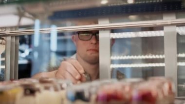 Down sendromlu beyaz bir adam bir kafede servis yapmak için buzdolabından tatlı alıyor. 8K 'da kırmızı helyum kamerayla çekildi.. 