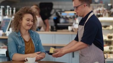 Caucasian male waiter with down syndrome serving a piece of cake in the cafe to the client at the table. Shot with RED helium camera in 8K. 