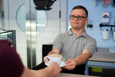 Down sendromlu beyaz bir adam müşteriye kahve servisi yapıyor.