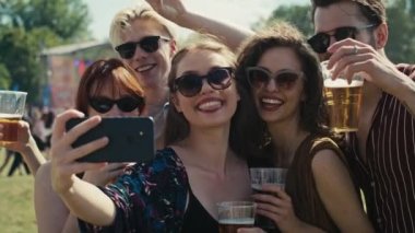 Bir grup beyaz arkadaş, müzik festivalinde ortak bir selfie için komik suratlar yapıyor. 8K 'da kırmızı helyum kamerayla çekildi.. 