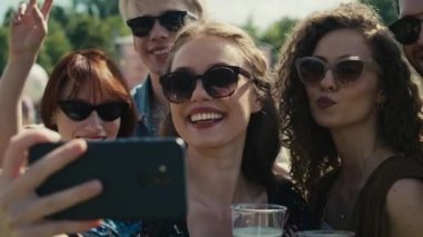 Bir grup beyaz arkadaş, müzik festivalinde ortak bir selfie için komik suratlar yapıyor. 8K 'da kırmızı helyum kamerayla çekildi.. 