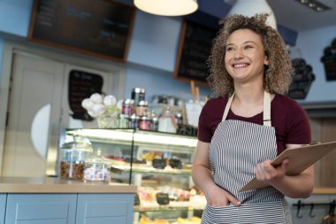Kafenin içinde önlük giymiş beyaz garson ve elinde menü var.