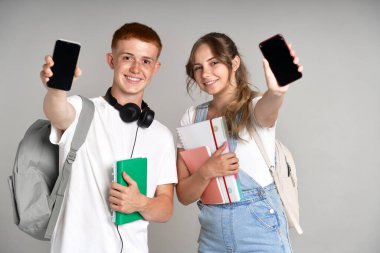 Gri arkaplanda cep telefonunu kameraya gösteren genç öğrenciler