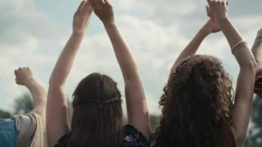 Rear view of friends dancing on music festival with hands up. Shot with RED helium camera in 8K.