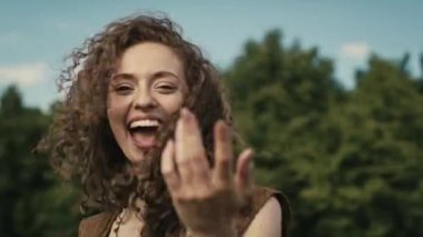 Kamera, müzik festivalinde kıvırcık saçlı, gülümseyen beyaz kadını izliyor. 8K 'da kırmızı helyum kamerayla çekildi.. 