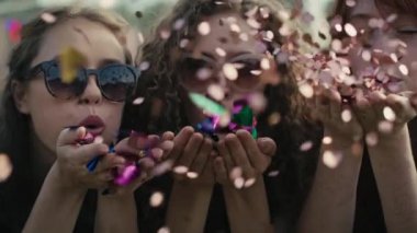 Three young caucasian females blowing confetti towards the camera and and later dance. Shot with RED helium camera in 8K. 