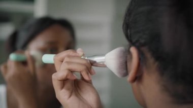 Afro-Amerikalı bir kadın banyoda makyaj kızartıcı sürüyor. 4K 'da kırmızı helyum kamerayla çekildi..     