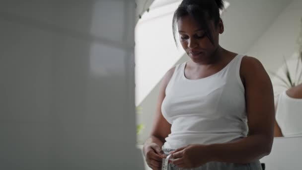 Dissatisfied African American Woman Standing Bathroom Taking Measures Her Waist — Vídeos de Stock