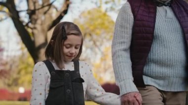 Beyaz küçük kız büyükbabasıyla parkta yürüyor. 4K 'da kırmızı helyum kamerayla çekildi.   