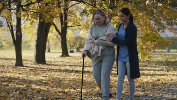 Young Female Nurse Helping Senior Woman Walking Park Shot Red — Vídeo de stock