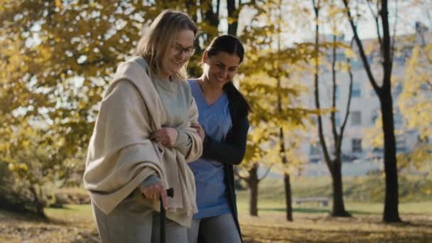 Young Female Nurse Helping Senior Woman Walking Park Shot Red — Vídeo de Stock