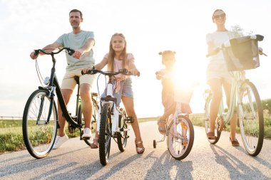 Family of four caucasian people sitting on bikes on village road 