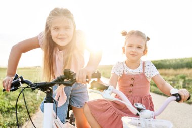Portrait of two little caucasian girls standing with their bikes at sunset time
