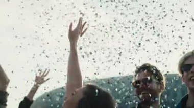Young caucasian friends dancing among confetti on music festival with hands up. Shot with RED helium camera in 8K. 