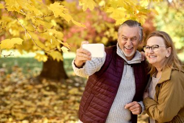 Senior woman and man making selfie at the park in autumn 