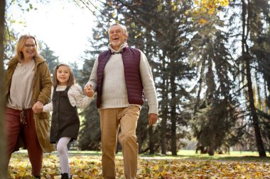Senior couple with granddaughter walking at the park during the autumn 