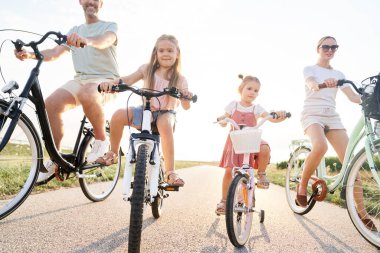 Family of four caucasian people sitting on bikes on village road 