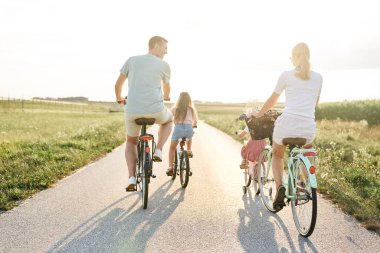 Rear view of family of four caucasian people riding bikes on village road 