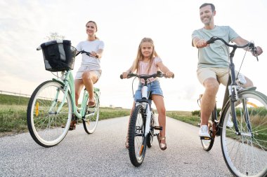 Family of three caucasian people riding bikes on village road 
