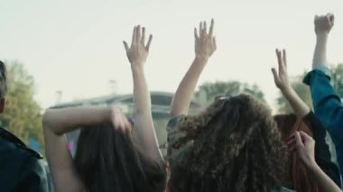Arkadaşların müzik festivalinde elleri havada dans edişinin arka görüntüsü. 8K 'da kırmızı helyum kamerayla çekildi..