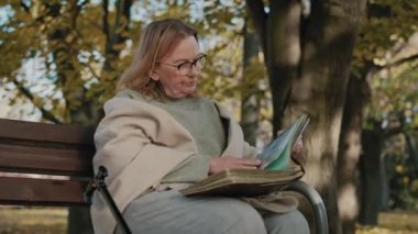 Senior woman sitting on bench and looking at old photographies. Shot with RED helium camera in 8K 