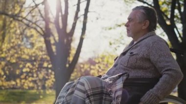 Senior man in a wheelchair on the move in park during the autumn. Shot with RED helium camera in 8K  