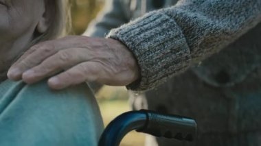 Close up of man touching hand of her wife which sitting on wheelchair. Shot with RED helium camera in 8K 
