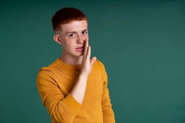 Caucasian teenage boy of ginger hair telling secret to the camera