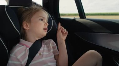 Caucasian girl of 6 years sitting in safety seat and looking out of the car window while car trip. Shot with RED helium camera in 8K.
