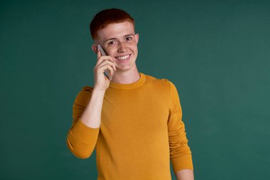 Caucasian ginger male teenager using mobile phone at green background