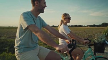 Cheerful caucasian couple of middle age riding a bike on sunset on village road. Shot with RED helium camera in 8K.   