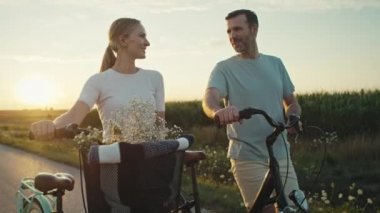Cheerful caucasian couple of middle age walking with a bike on sunset on village road. Shot with RED helium camera in 8K.   