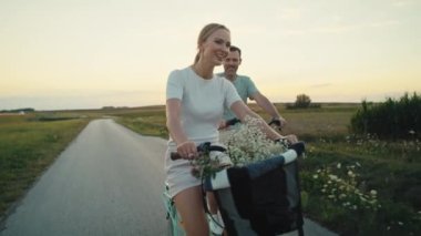 Front view of cheerful caucasian couple of middle age riding a bike on sunset on village road. Shot with RED helium camera in 8K.   