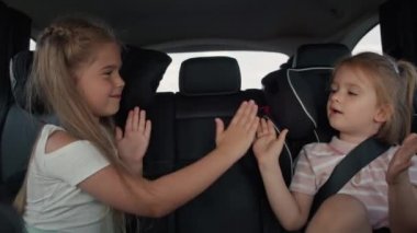 Two caucasian female children sitting on the back seat and playing clapping game. Shot with RED helium camera in 8K.