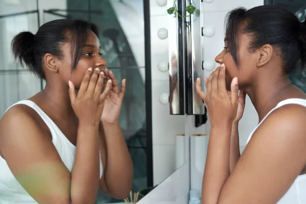 Side view of young African-American woman checking skin condition in the mirror in the morning