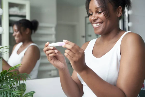 Happy African-American  woman holding pregnancy test results