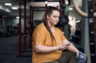 Woman with overweight using mobile phone at the gym