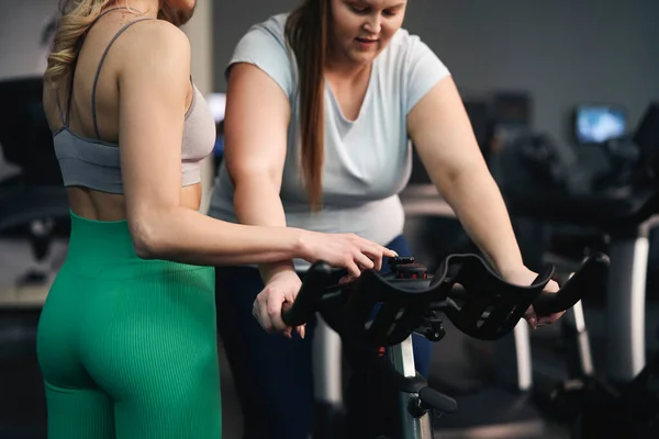 Caucasian instructor helping plus size woman at the gym