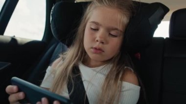 Caucasian girl of 6 years using mobile phone while riding in car. Shot with RED helium camera in 8K.