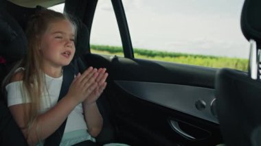 Female caucasian child singing and clapping hands while driving in the car . Shot with RED helium camera in 8K.