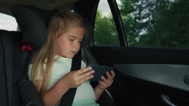 Caucasian girl of 8 years using mobile phone while riding in car. Shot with RED helium camera in 8K.