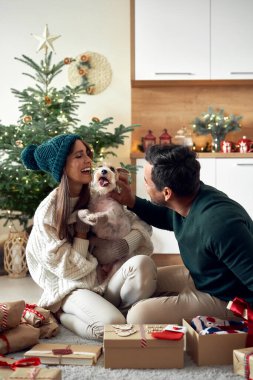 Happy couple opening Christmas presents with dog at home 