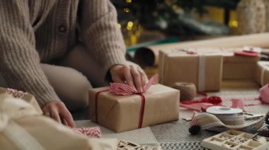 Tanınmayan beyaz bir kadın yere Noel hediyelerini paketliyor. 8K 'da kırmızı helyum kamerayla çekildi..    